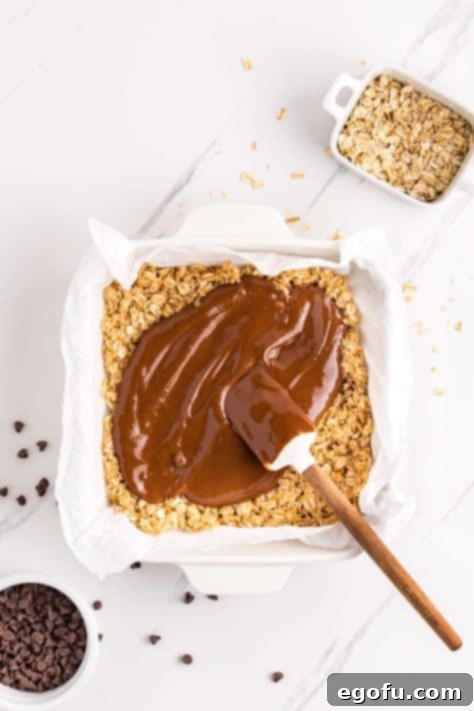 The rich chocolate peanut butter mixture being poured over the first oat layer in the baking dish.