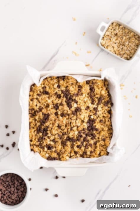 Mini chocolate chips being sprinkled generously over the top layer of the oatmeal bars.