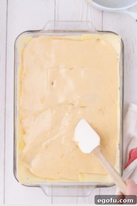 Golden Baked Chicken Ham and Swiss Casserole 19 A rubber spatula smoothing a creamy sauce in a baking dish.