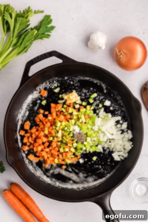 A cast iron skillet with butter, oil, onion, carrots, celery, garlic, black pepper, and salt.