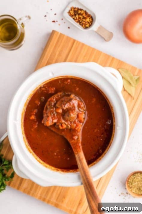 A wooden spoon holding some Ragu in crockpot.