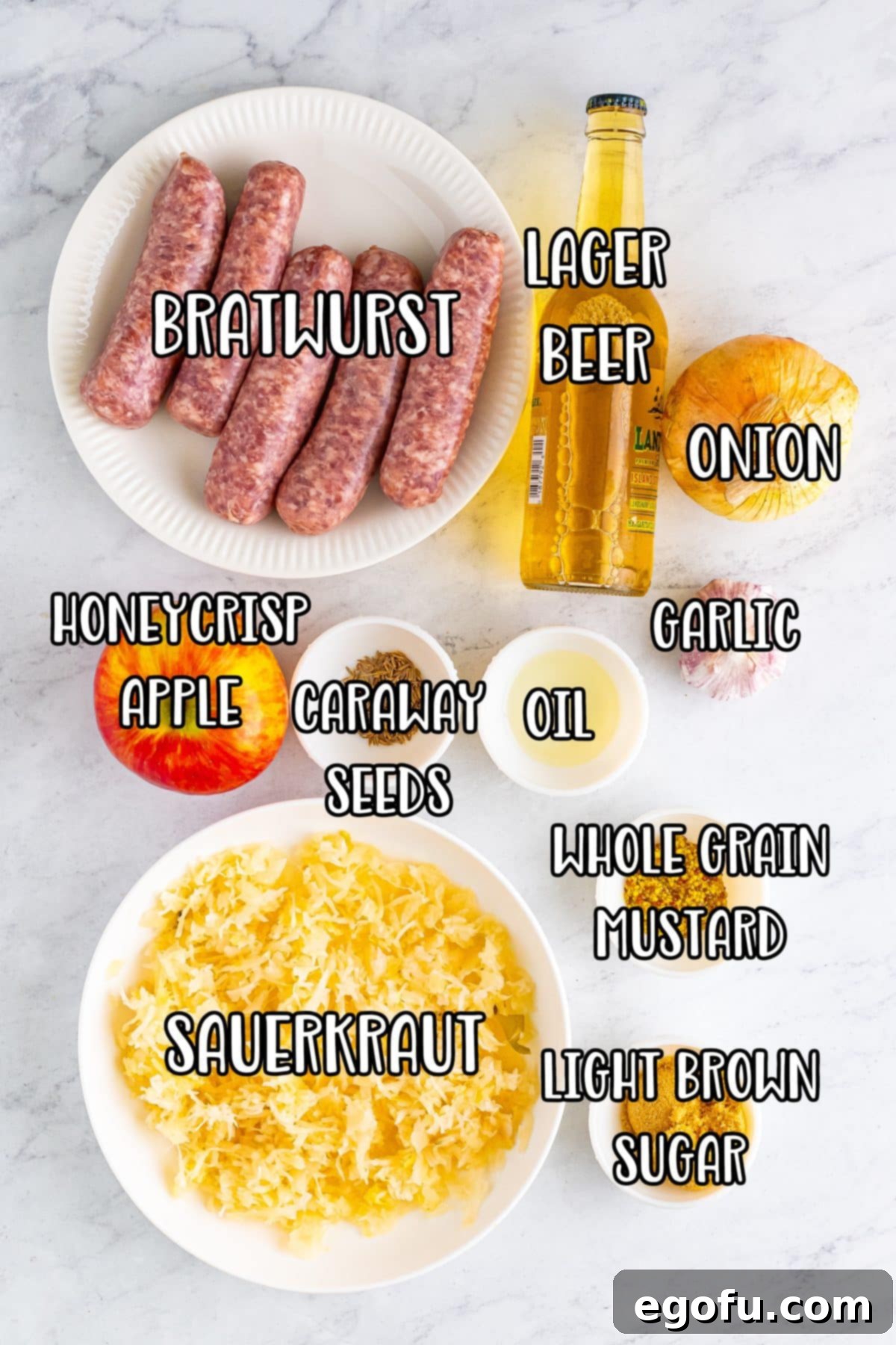 Hearty Slow Cooker Brats with Sauerkraut 4 A flat lay of all the fresh ingredients for Slow Cooker Brats: bratwurst, vegetable oil, sweet onion, garlic cloves, sauerkraut, honey crisp apple, lager beef, light brown sugar, whole grain mustard, and caraway seeds.