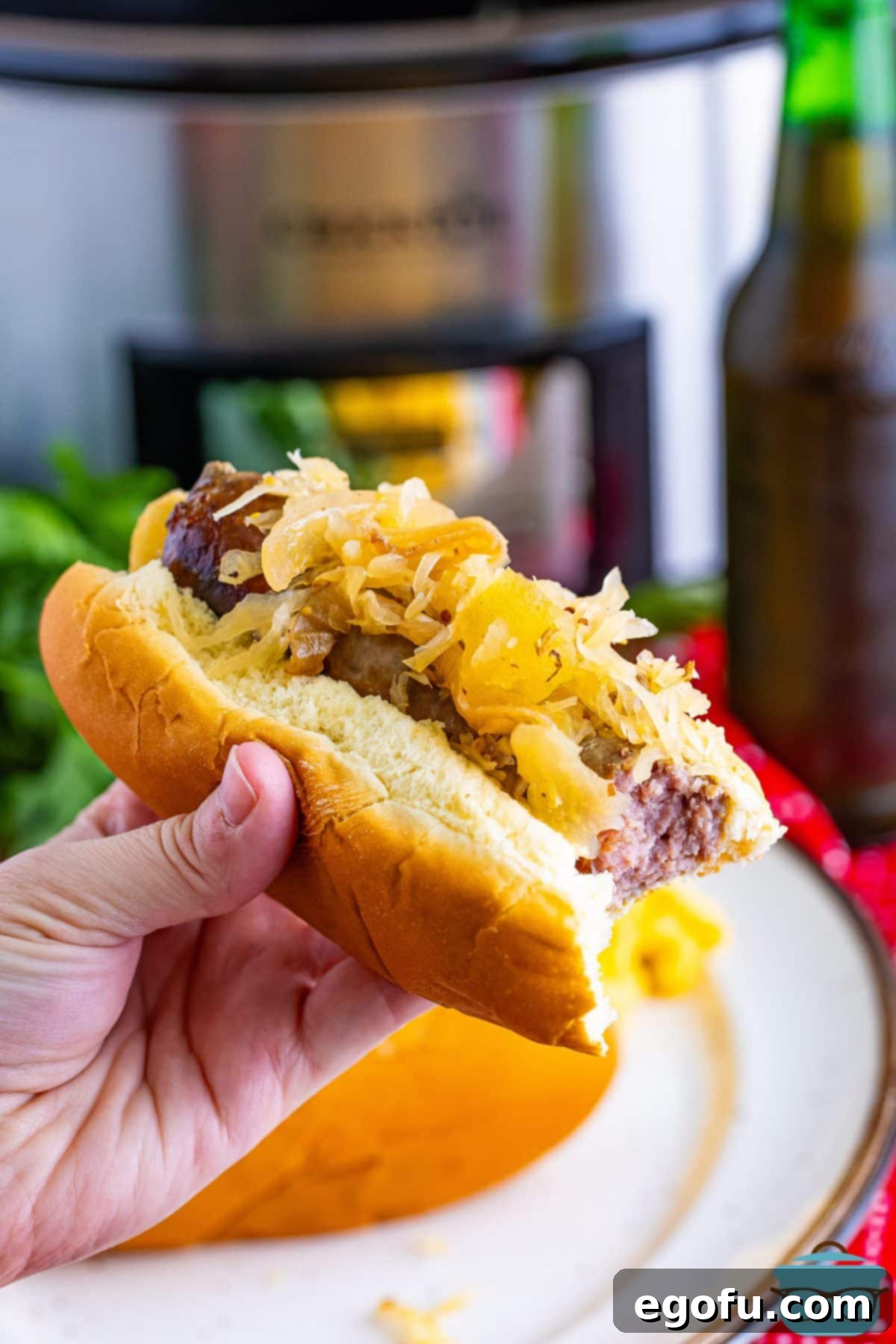 Hearty Slow Cooker Brats with Sauerkraut 8 A hand holding a hot dog bun with a Slow Cooker Brat, ready to be eaten.