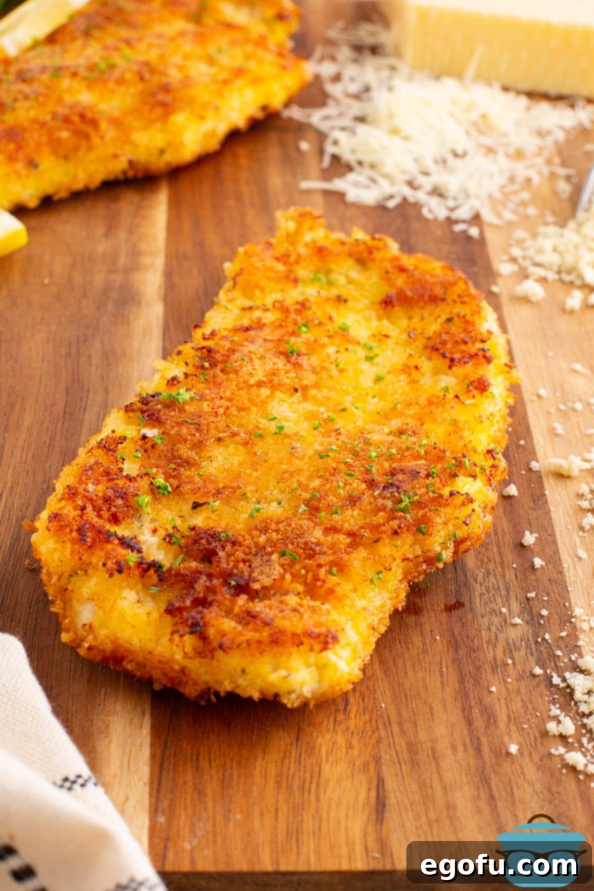 Crispy Parmesan Chicken Delight 2 A Parmesan Crusted Chicken piece on a cutting board, showcasing its perfectly golden-brown and crispy crust.