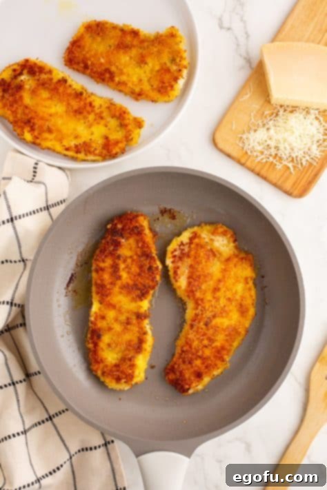 Crispy Parmesan Chicken Delight 12 Two fried pieces of Parmesan Crusted Chicken sizzling in a skillet to a golden brown.