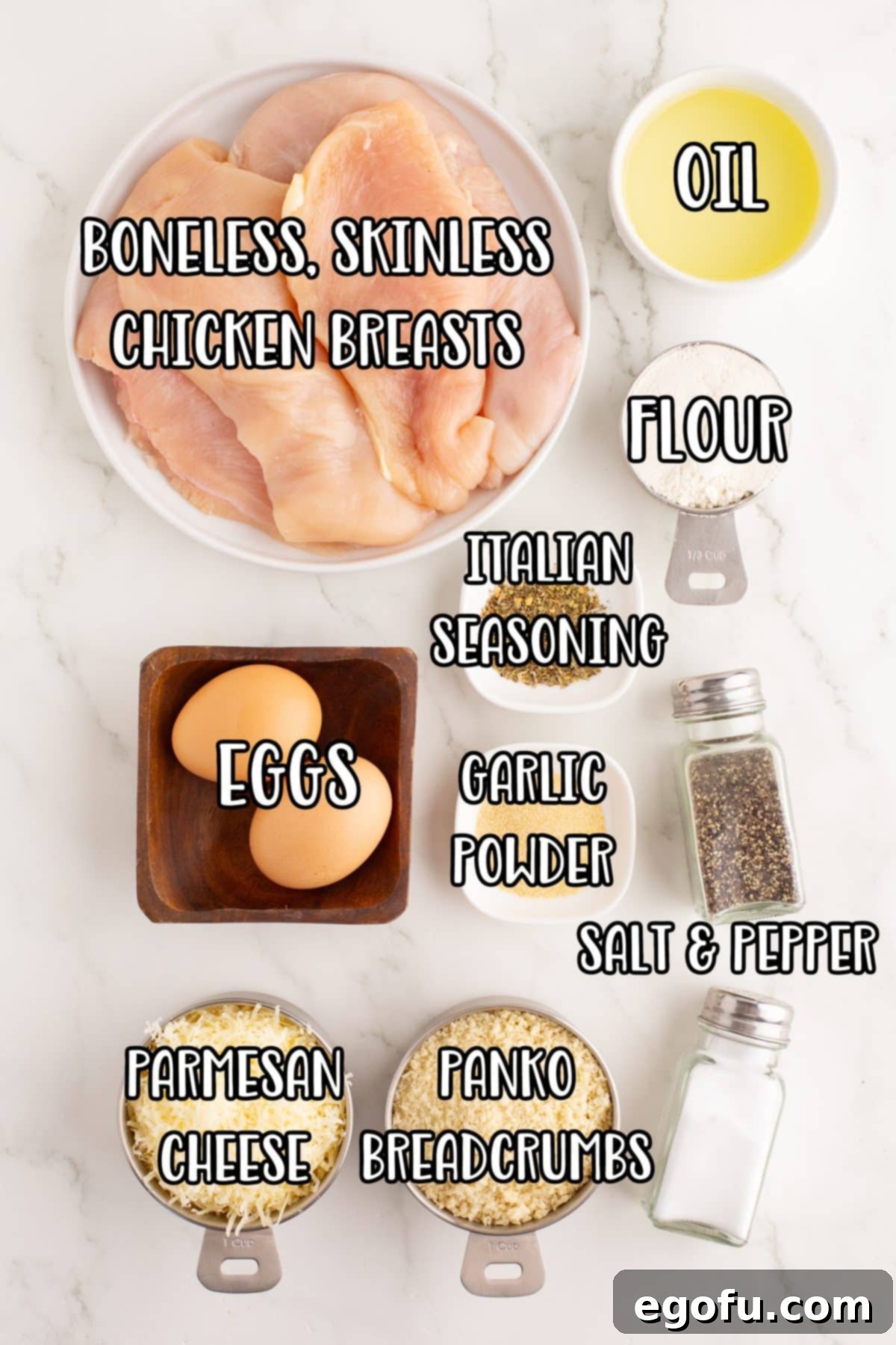 Crispy Parmesan Chicken Delight 4 A flat lay of all ingredients meticulously laid out for Parmesan Crusted Chicken: boneless skinless chicken breasts, a bottle of oil, eggs, a bowl of flour, parmesan cheese, salt, pepper, garlic powder, Italian seasoning, and a bowl of panko bread crumbs.