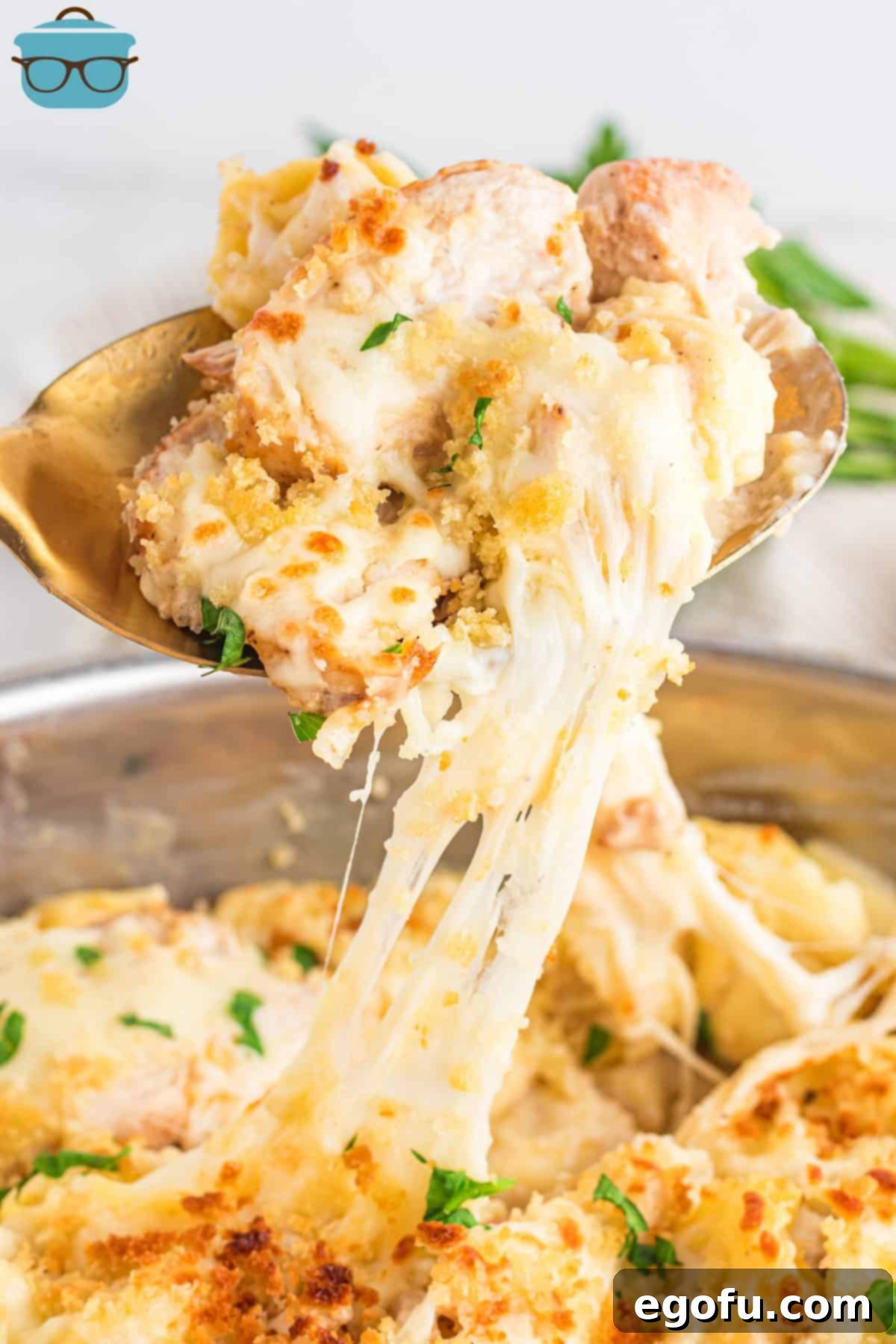 A serving utensil lifting a generous portion of golden-brown Chicken Alfredo Tortellini, showcasing the creamy sauce and melted cheese.