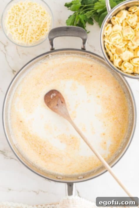 A wooden spoon in Alfredo sauce in a skillet.