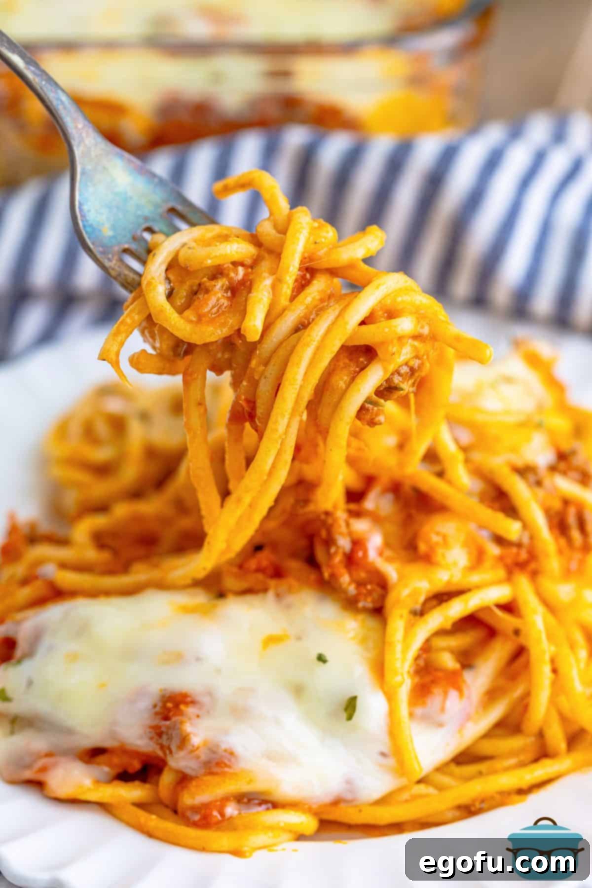 A plate of Baked Spaghetti for Two with a fork holding a bite, showcasing the melted cheese and rich sauce.
