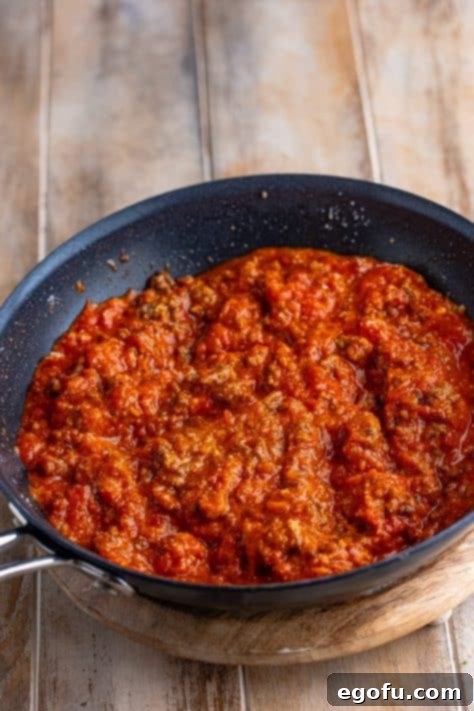 Marinara sauce combined with seasoned ground beef in a skillet.