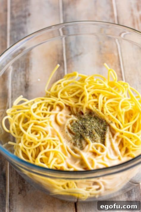 Spaghetti mixed with Alfredo sauce and Italian seasoning in a bowl.
