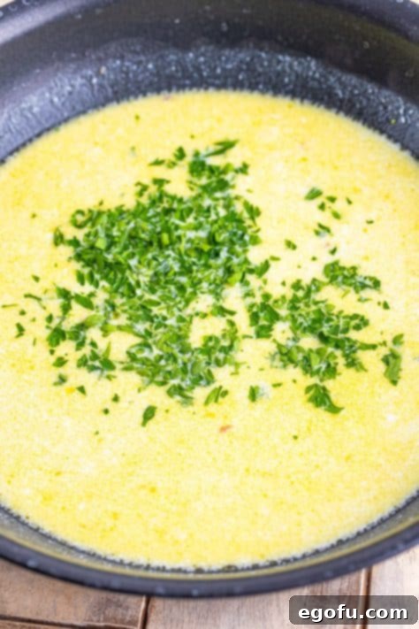 Zesty Piccata Chicken Bites 21 Parsley and lemon juice added to cream sauce in a pan.