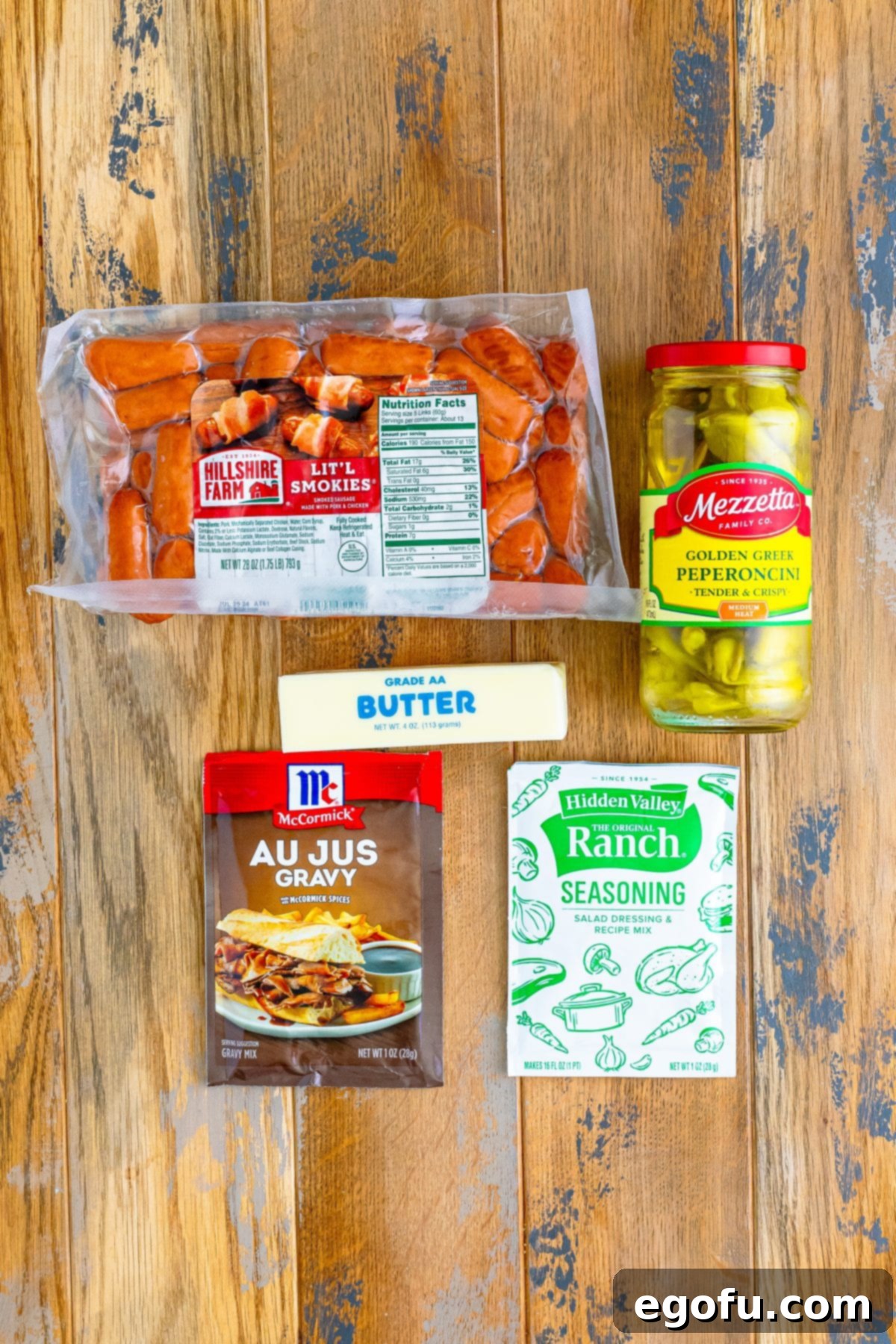 Irresistible Slow Cooker Mississippi Sausages 4 Individual ingredients neatly laid out: Lit'l Smokies, au jus gravy mix, ranch seasoning mix, whole pepperoncini peppers and their juice, and unsalted butter.