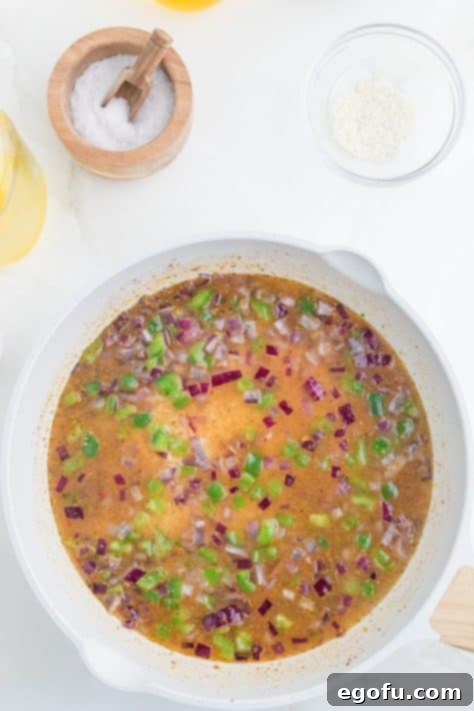 Red onions, peppers, broth, and spices in a skillet.