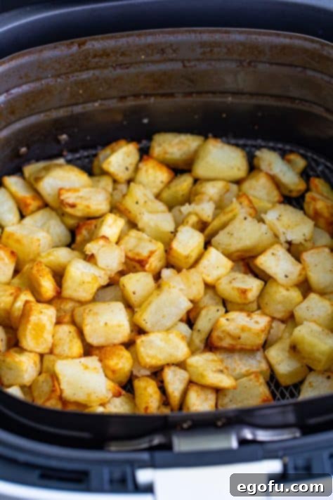 Cooked diced potatoes in an air fryer basket, golden brown and crispy.