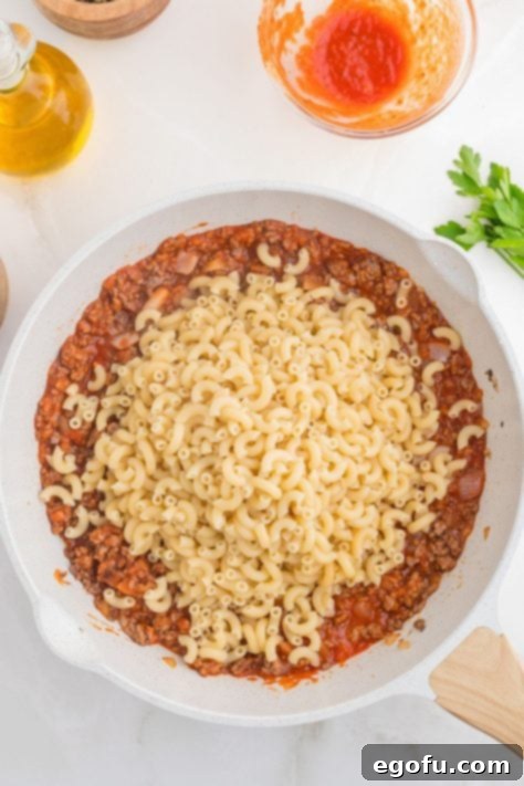 Macaroni pasta, tomato sauce, ground beef, and onion in a skillet.