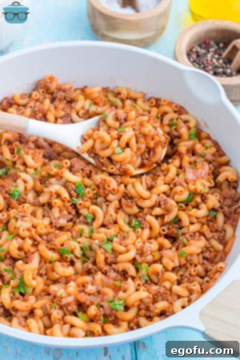 A wooden spoon in a skillet of Beefaroni.