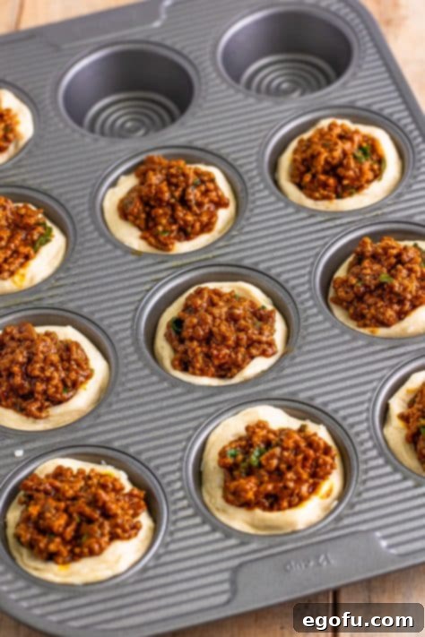 Ground beef and biscuit dough in a muffin tin.