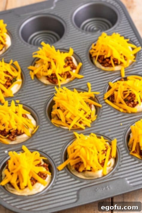 Shredded cheese on top of ground beef in a biscuit cup.