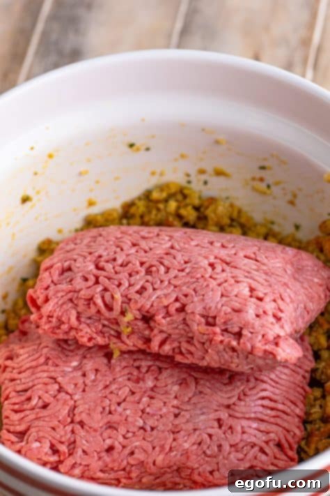 Lean ground beef being carefully placed into the bowl with the prepared stuffing, egg, and Worcestershire mixture, poised for gentle mixing by hand.