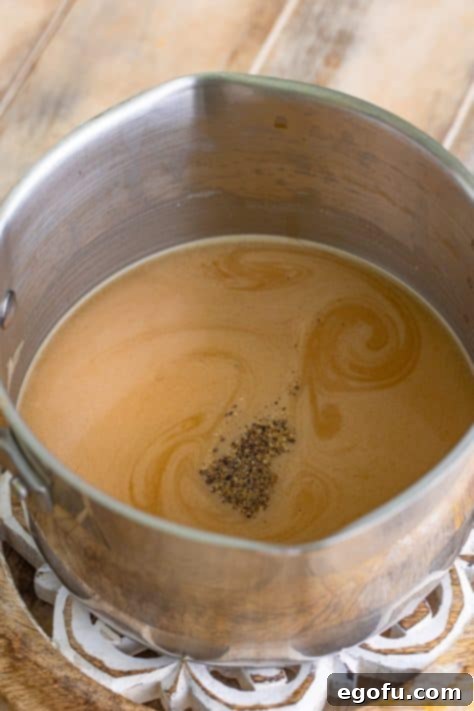 The simmering gravy in a pot, seasoned with Worcestershire sauce and black pepper, ready to be whisked for full flavor integration.