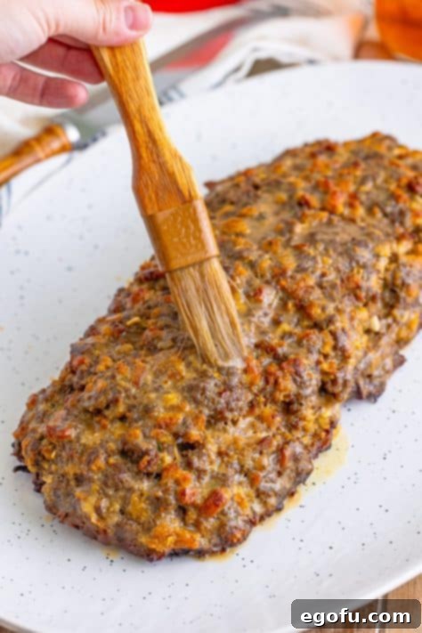 A culinary brush generously applying savory gravy over the entire surface of the baked Stove Top Stuffing Meatloaf, enhancing its appearance and flavor.