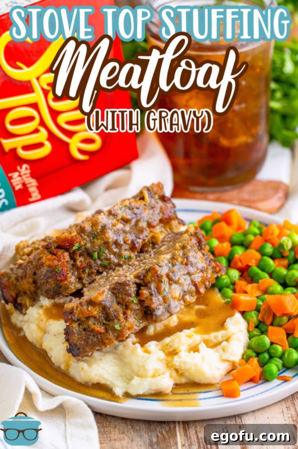 A comforting plate featuring a generous slice of Stove Top Stuffing Meatloaf, drizzled with gravy, served over a bed of mashed potatoes, accompanied by vibrant green peas and tender carrots.