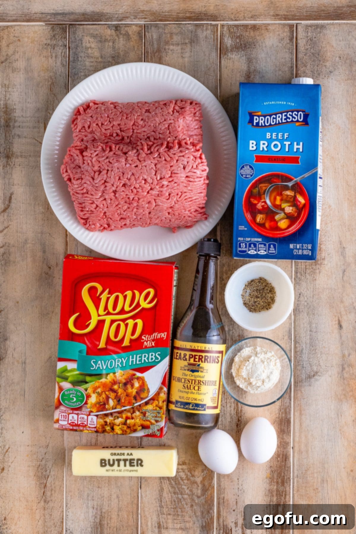 A vibrant flat lay image showcasing all the key ingredients for Stove Top Stuffing Meatloaf: lean ground beef, a box of stuffing mix, beef broth, large eggs, Worcestershire sauce, black pepper, butter, and all-purpose flour.