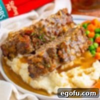 Close-up view of several slices of Stove Top Stuffing Meatloaf, generously covered in gravy, nestled atop a mound of mashed potatoes on a plate.