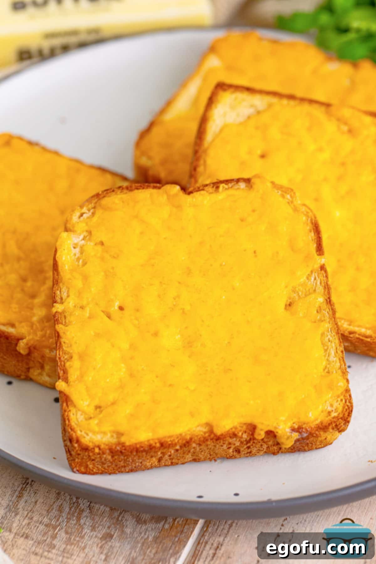 A few slices of perfectly golden and bubbly Cheese Toast on a white plate, ready to be served.