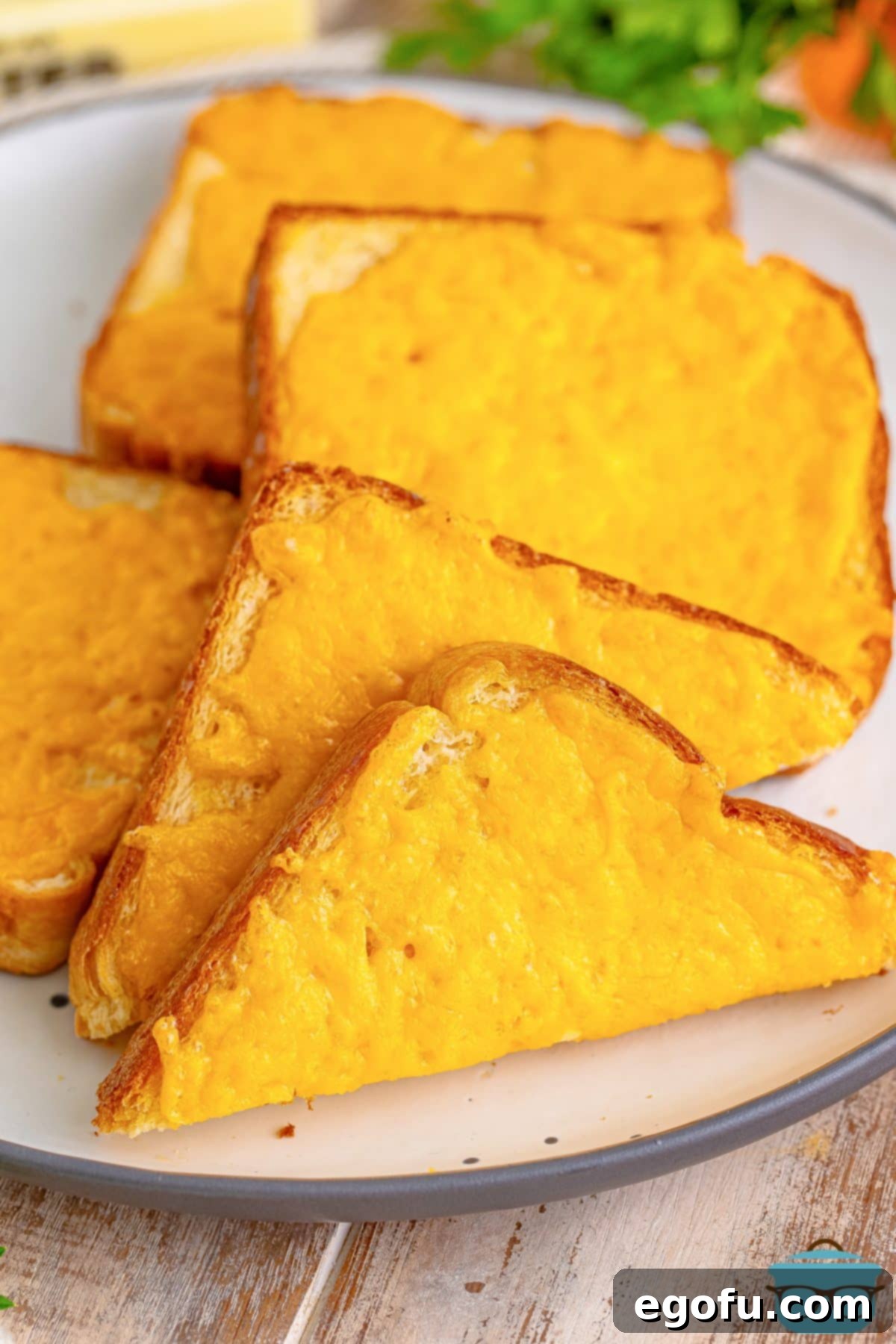 A plate of freshly baked Cheese Toast, with one slice cut in half to show the gooey melted cheese interior.