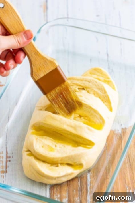 Melted butter being brushed on a raw bread loaf.