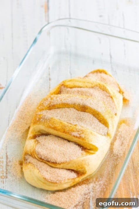 Cinnamon and sugar mixture on a slitted raw bread loaf.