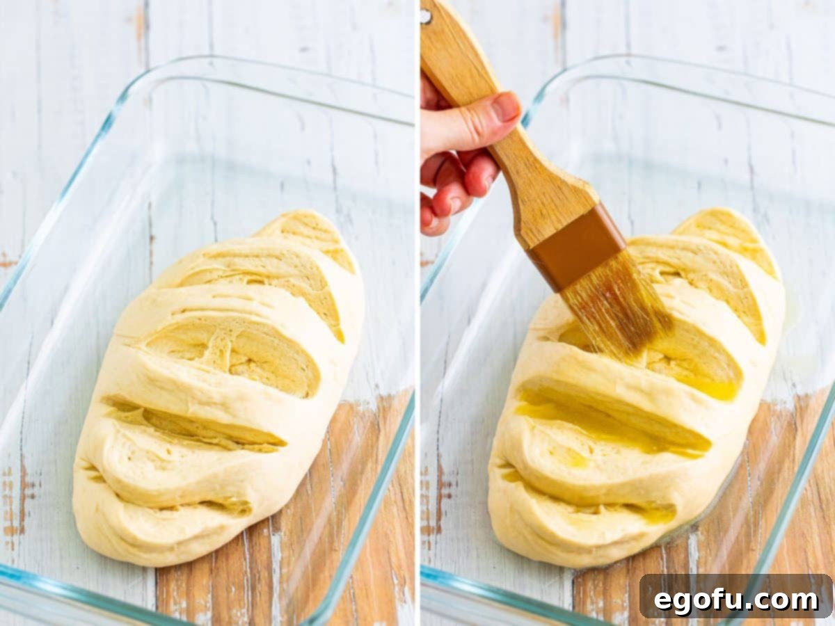 A thawed bread loaf with five deep slits, being generously brushed with melted butter.