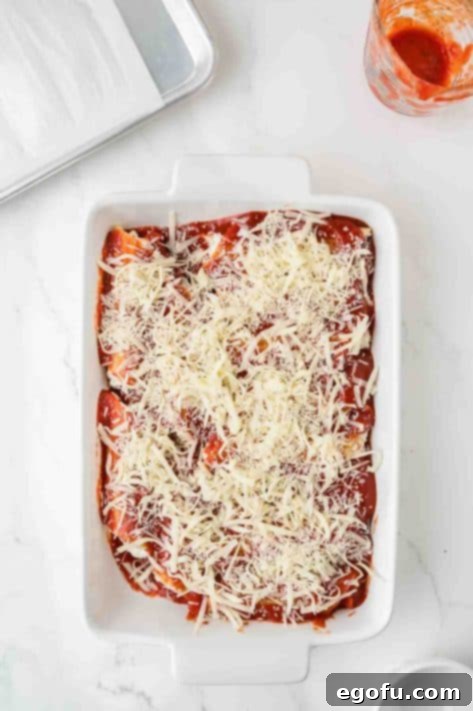 Effortless Manicotti 13 Marinara and cheese on top of stuffed manicotti shells in a baking dish.