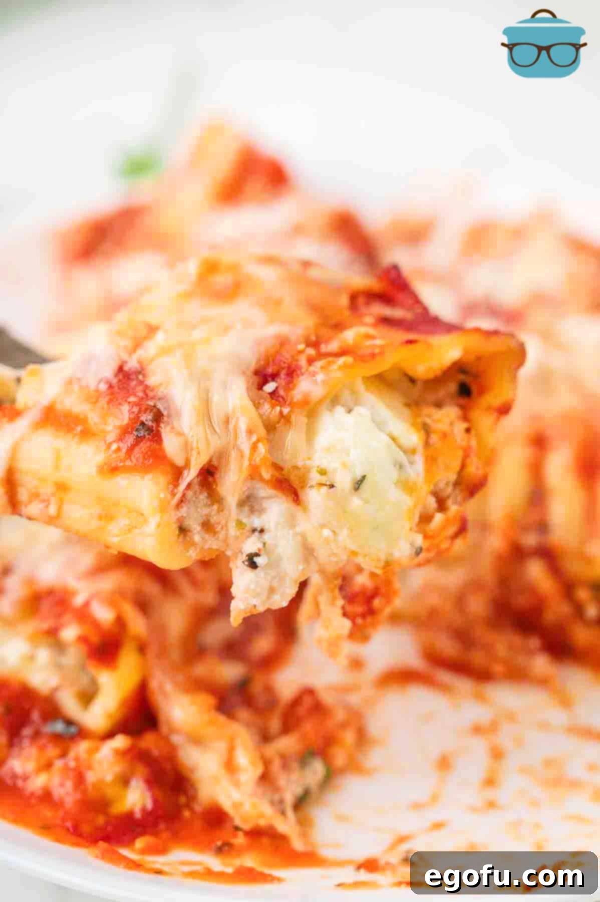 Effortless Manicotti 8 A fork lifting a perfect bite of Easy Manicotti from a plate, showcasing the rich filling, sauce, and melted cheese.