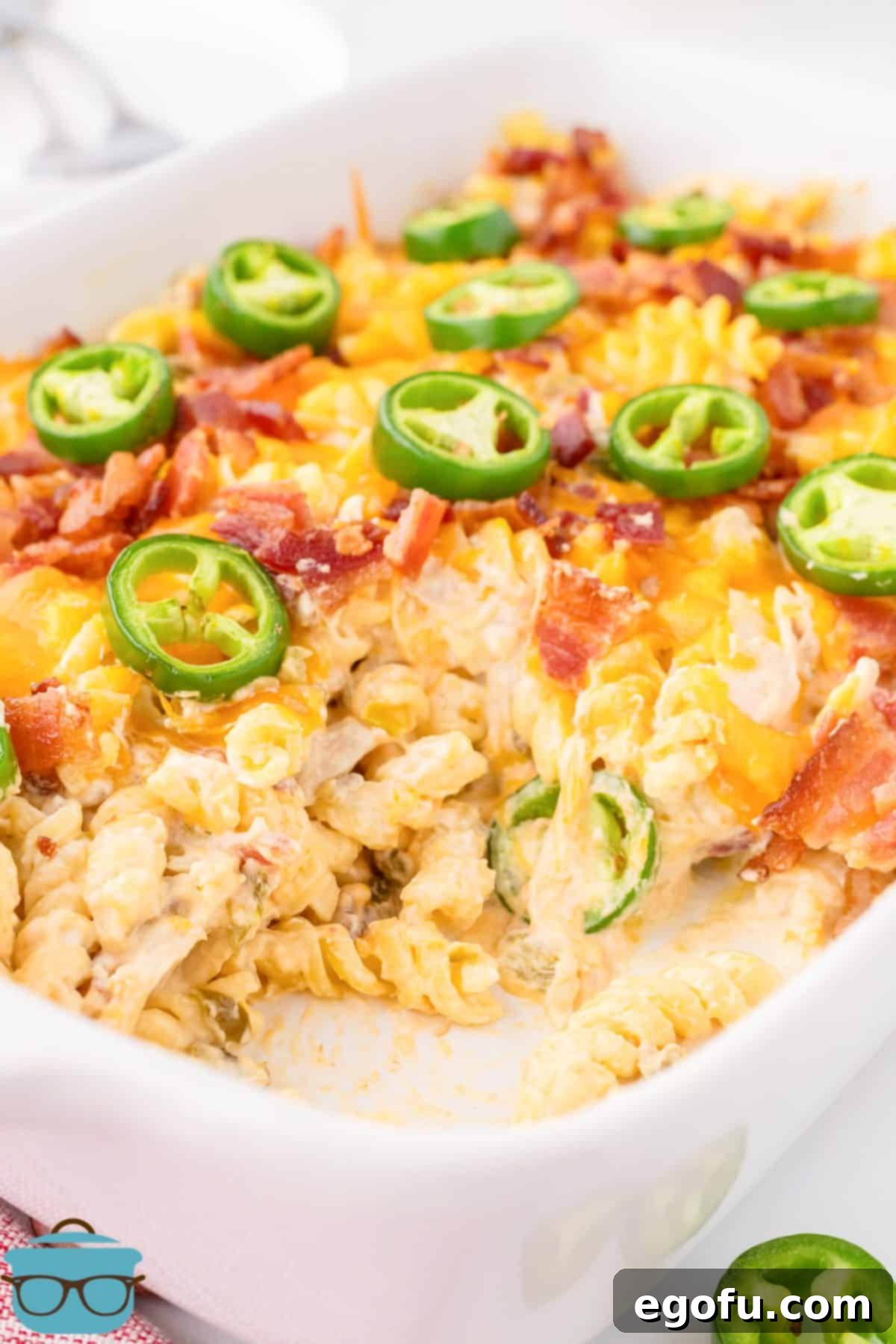 A baking dish with a Chicken casserole with jalapeno popper flavors. Golden brown and bubbly, with visible chicken, pasta, bacon, and cheese, topped with fresh jalapeño slices.