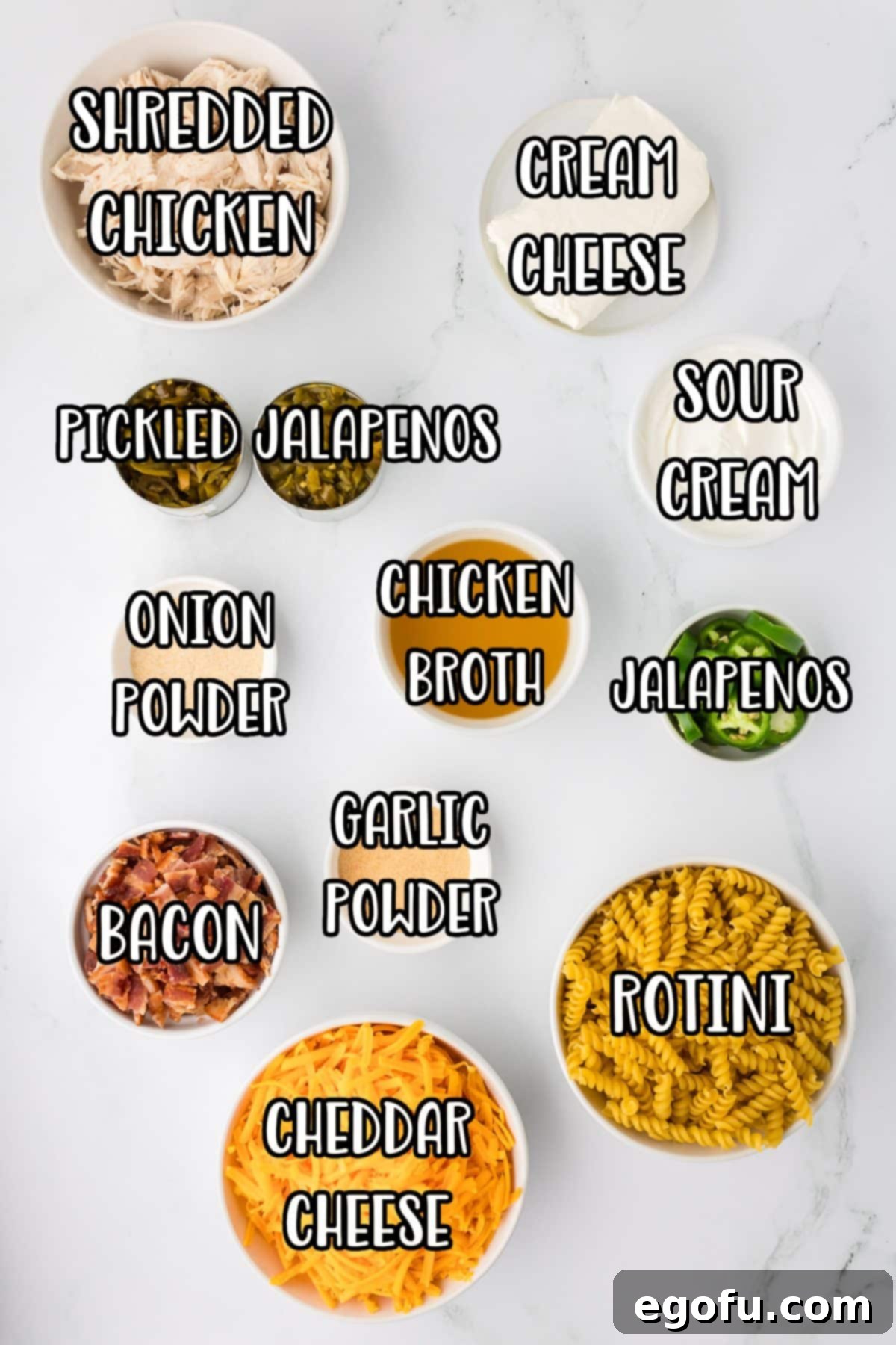 A vibrant flat lay showcasing all the ingredients for Chicken Jalapeno Popper Casserole: Rotini, chicken broth, bacon, garlic powder, onion powder, canned and fresh jalapenos, sour cream, cheddar cheese, cream cheese, and cooked chicken breasts.
