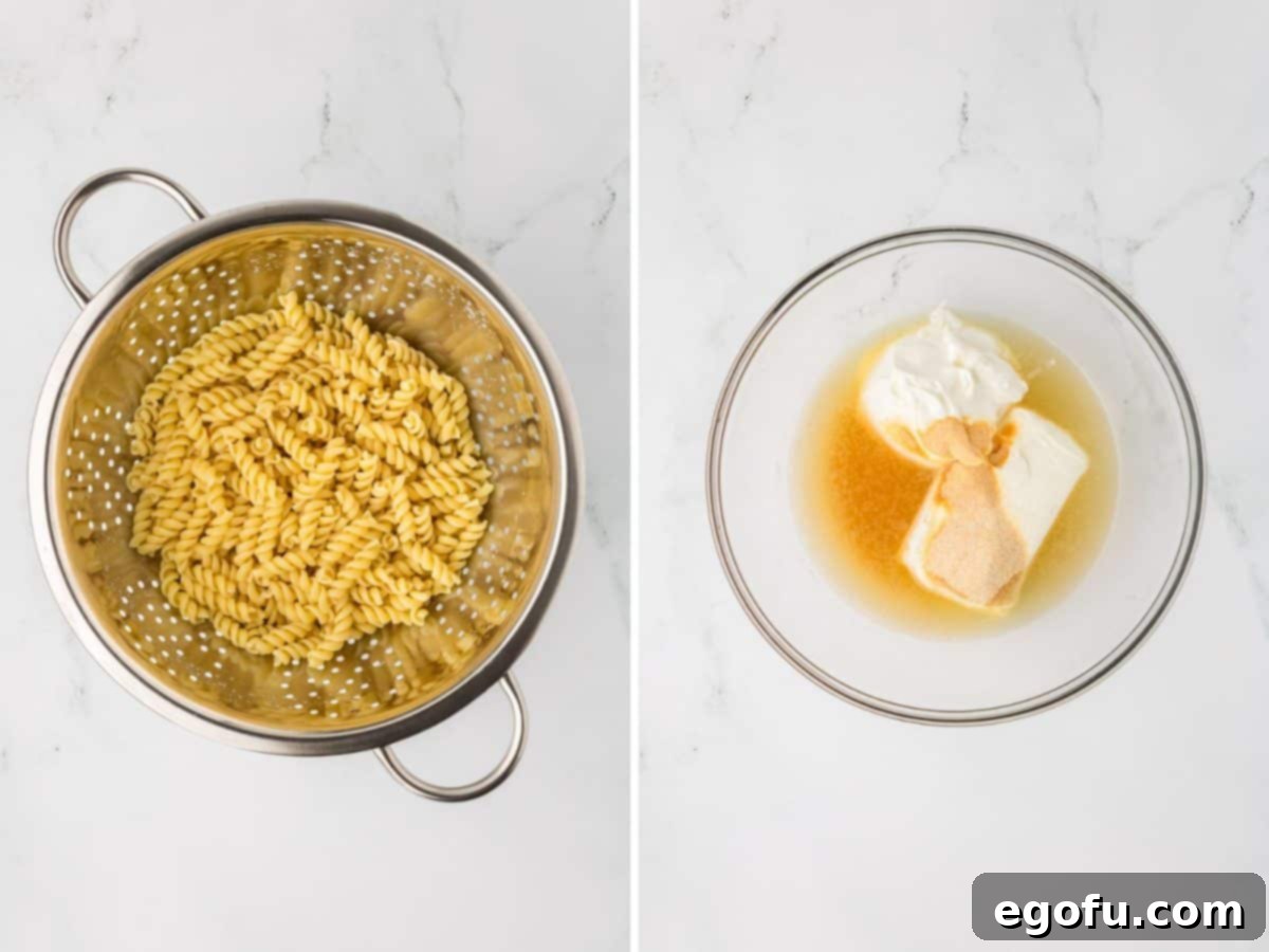 A strainer with freshly boiled rotini pasta alongside a mixing bowl containing softened cream cheese, chicken broth, sour cream, garlic powder, and onion powder.