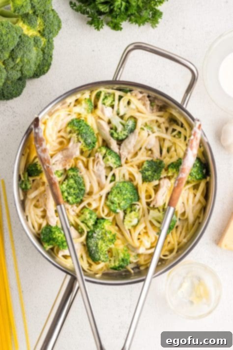 Chicken, pasta, and broccoli being tossed with Alfredo sauce in a pan.