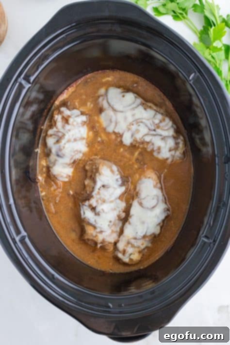 Melted cheese on top of chicken in a slow cooker.