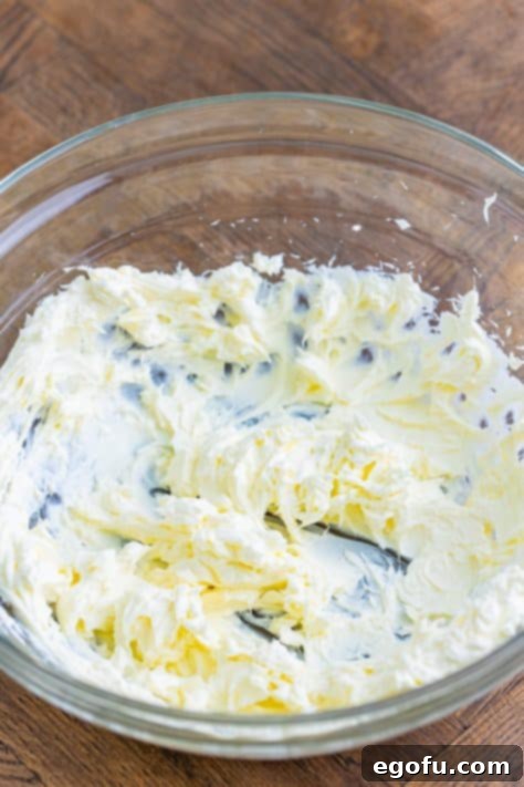 Cream cheese in a bowl being whipped with an electric mixer.
