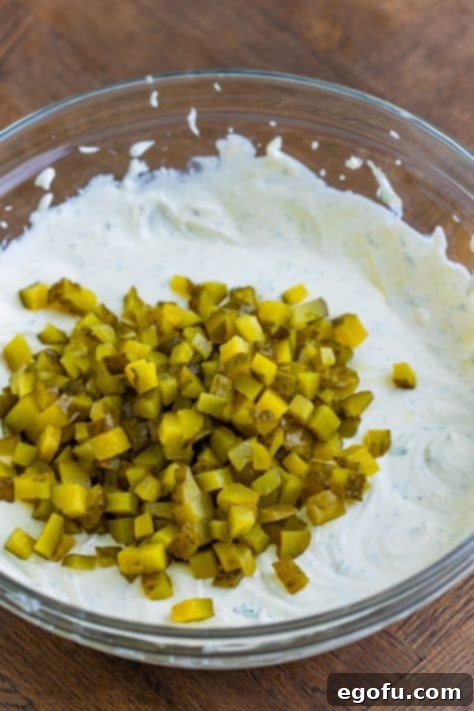 Dill pickles being gently stirred into the creamy ranch dip.