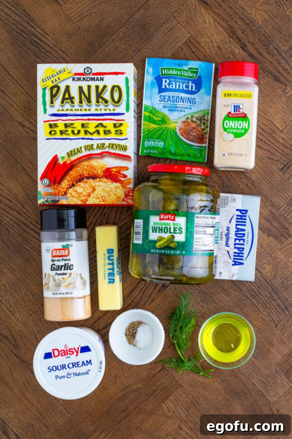 All the fresh ingredients for Fried Pickle Dip laid out on a wooden surface, including sour cream, panko breadcrumbs, pickles, pickle juice, cream cheese, garlic powder, onion powder, ranch seasoning mix, fresh dill, salt, and pepper.