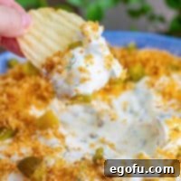 A chip being dipped into creamy Fried Pickle Dip, showcasing its texture and the golden brown topping.