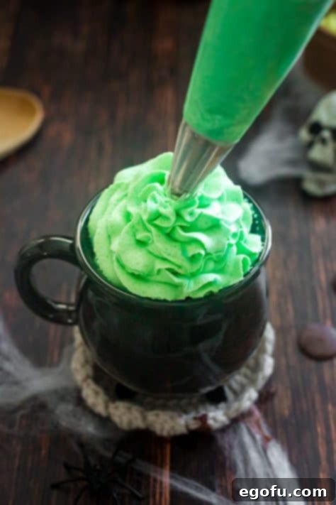 Bewitching Brew Hot Chocolate 12 Green whipped topping being piped onto a mug of hot cocoa, creating a festive swirl.