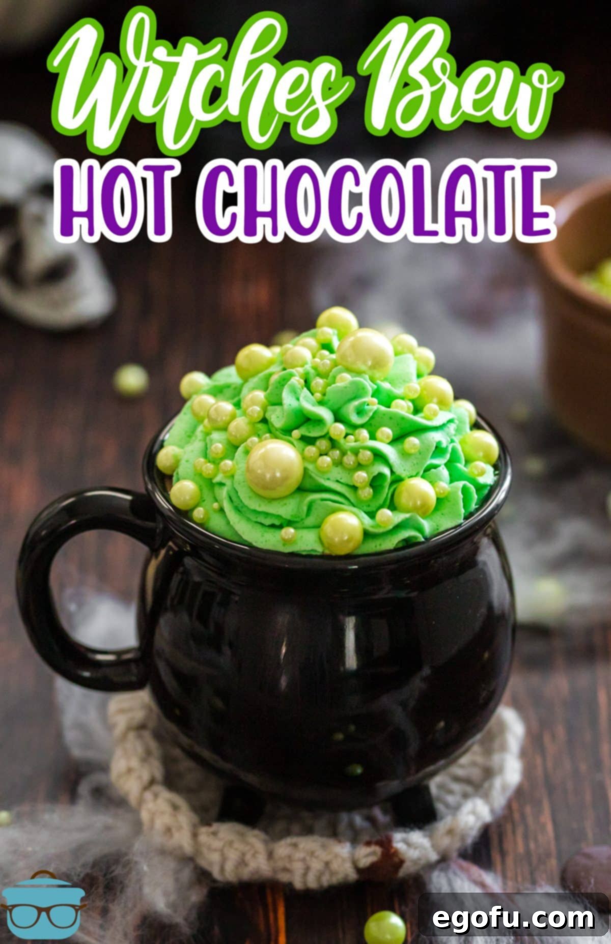 Bewitching Brew Hot Chocolate 3 A black cauldron mug filled with Witches Brew Hot Chocolate, topped with a generous swirl of green whipped cream and a sprinkle of green spheres.