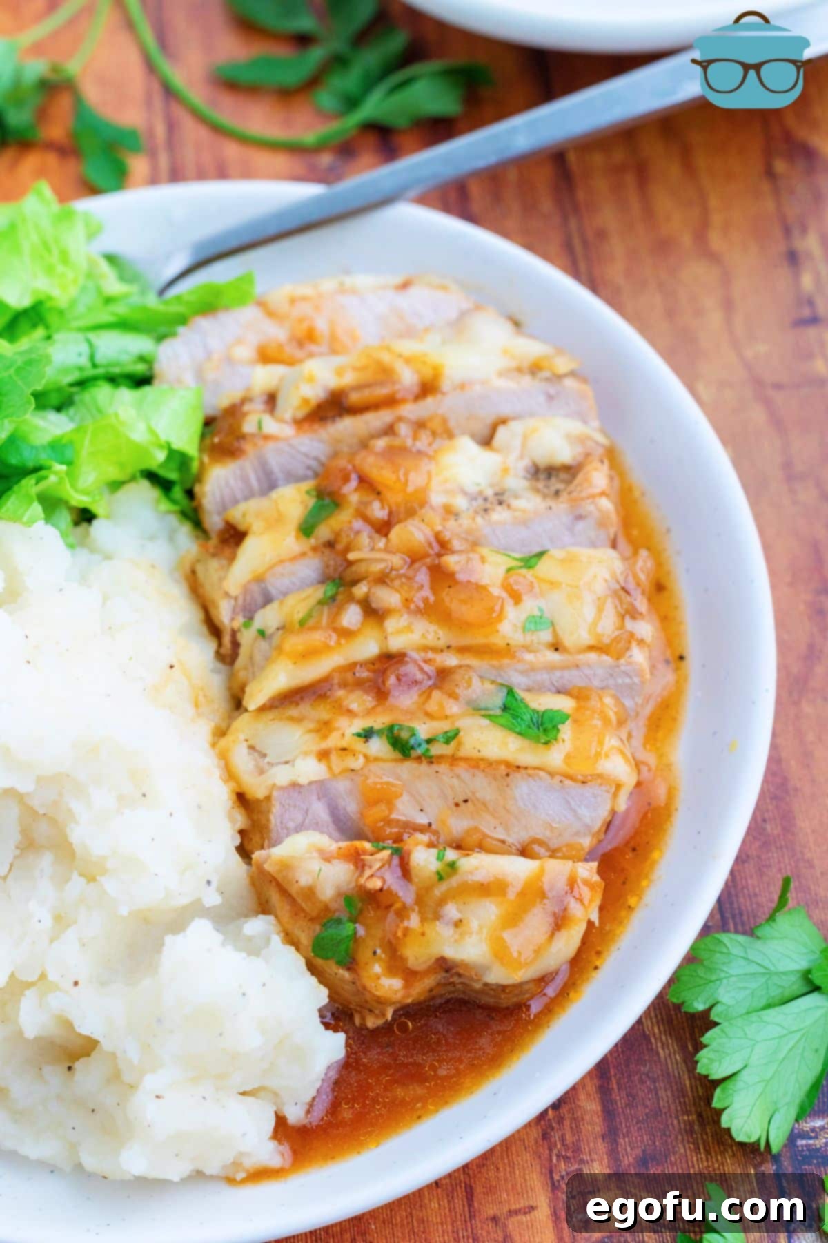 Caramelized Onion Smothered Pork Chops 2 A plate with a sliced up pork chop with french onion gravy and a side of mashed potatoes.