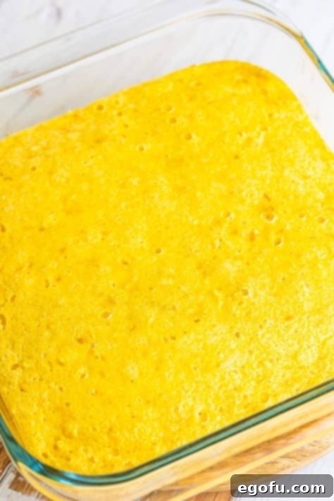 A baking dish containing a freshly baked, golden-brown cornbread crust, ready for the next layer of the Tamale Pie.