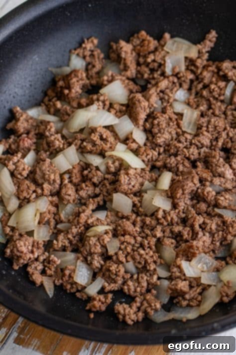 A skillet filled with ground beef and diced onions cooking over medium-high heat, browning the meat for the Tamale Pie filling.